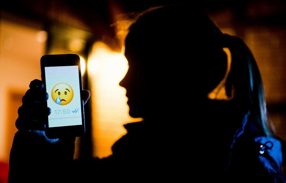 DOSSIER - Une jeune femme montre un emoji qui pleure sur l'écran de son mobile. Photo : Julian Stratenschulte/dpa