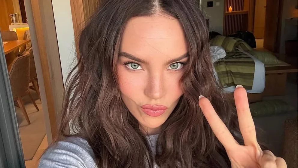 Gros plan de Belinda avec des cheveux châtain ondulés et une raie au milieu, des yeux verts, des lèvres avec du brillant rose et faisant un signe de paix de la main droite