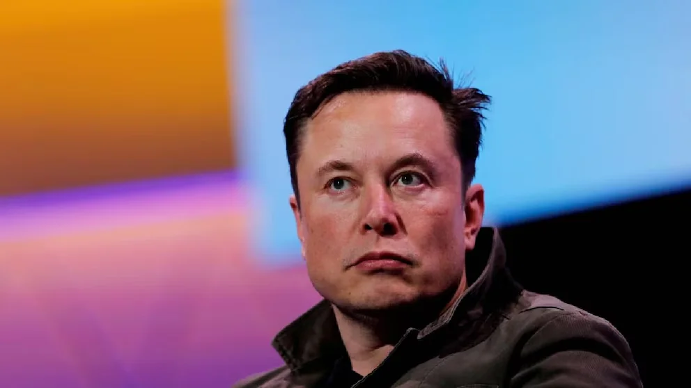 Gros plan d'Elon Musk, homme aux cheveux foncés, regardant vers la droite. Il porte une veste sombre. Fond flou avec des dégradés d'orange, violet et bleu