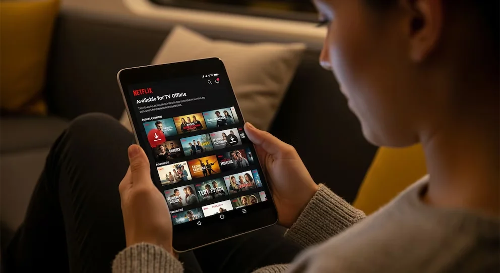 Une personne tient une tablette affichant l'application Netflix, avec la section 