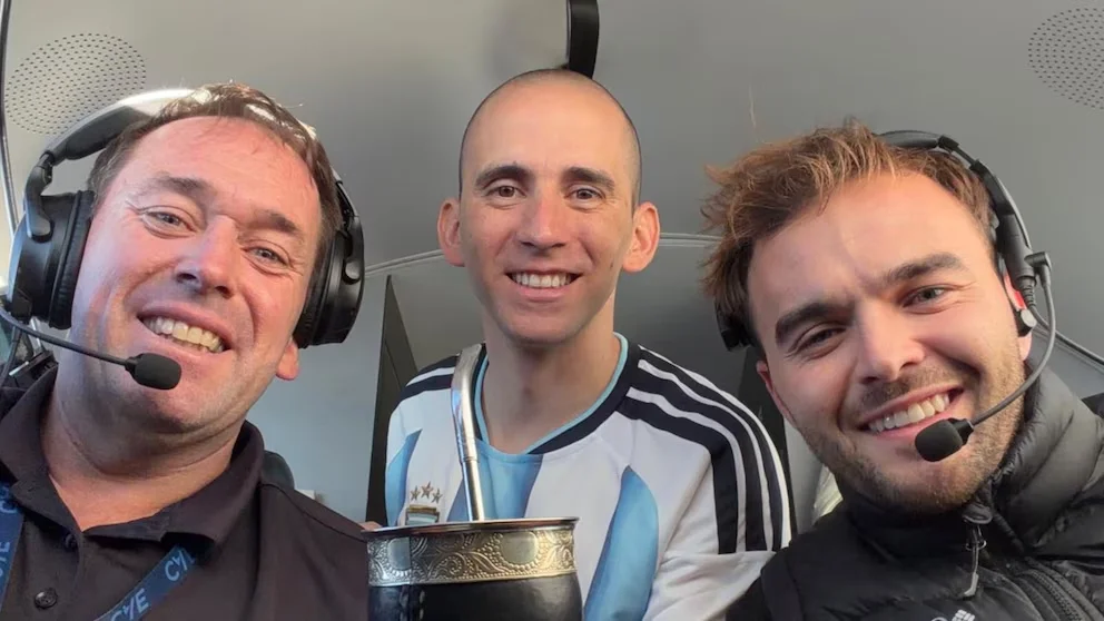 Trois hommes souriant, deux avec des écouteurs et des microphones, à l'intérieur d'un avion ; celui du centre, Nahuel Gallo, en t-shirt de l'Argentine et portant un mate