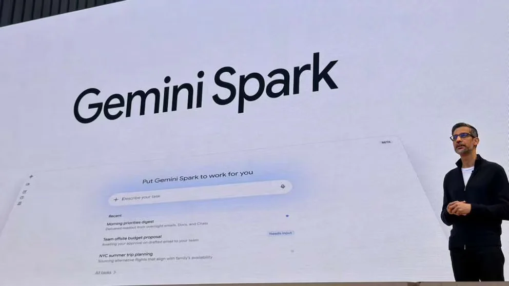 Sundar Pichai, avec des lunettes et un pull sombre, debout devant un grand écran affichant le logo