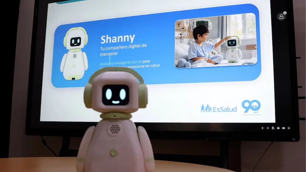 Un robot rose avec des écouteurs verts en gros plan devant un écran affichant des informations sur le robot Shany et la photo d'un enfant interagissant avec un autre robot dans un hôpital