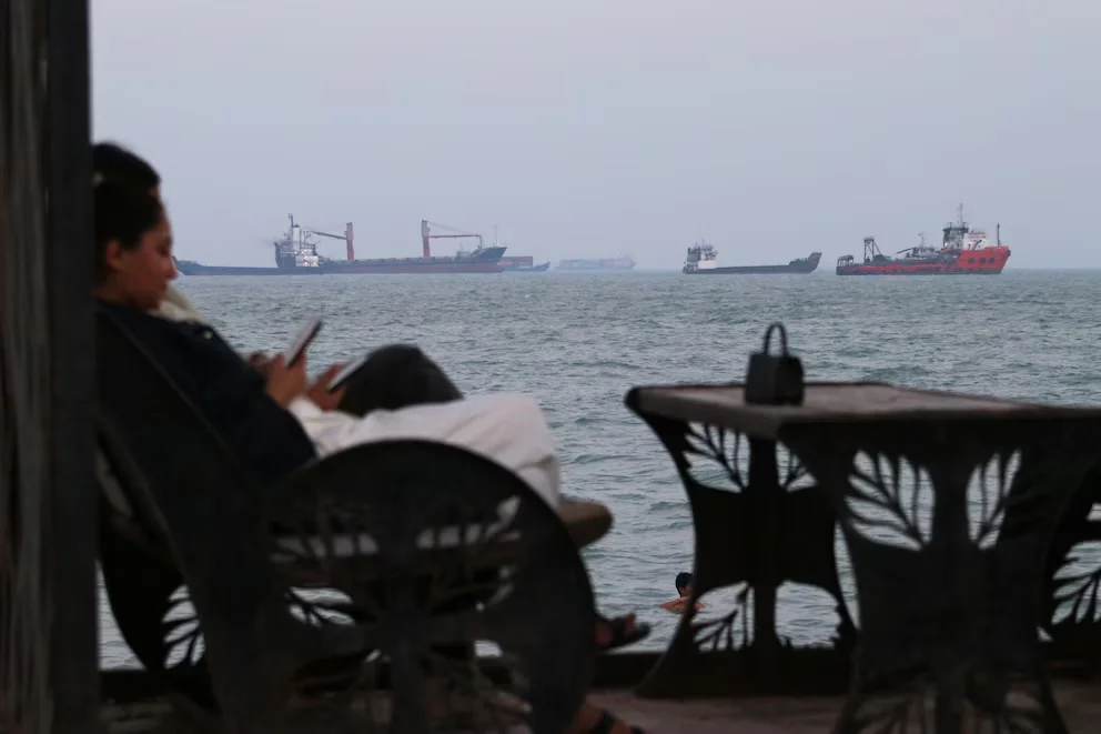 Deux personnes consultent leurs téléphones dans un café avec vue sur les navires marchands dans le détroit d'Ormuz, le dimanche 12 juillet 2026, en face de Bandar Abbas, Iran (Razieh Poudat/ISNA via AP)